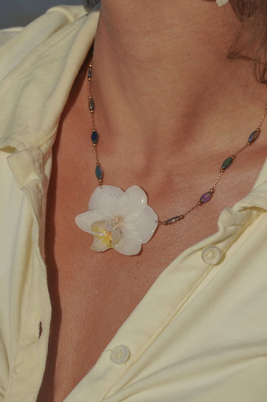 Necklace with a white orchid pendant worn by a person in a light-colored shirt.